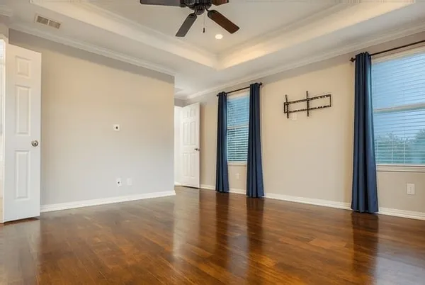 a view of an empty room with wooden floor and a ceiling fan