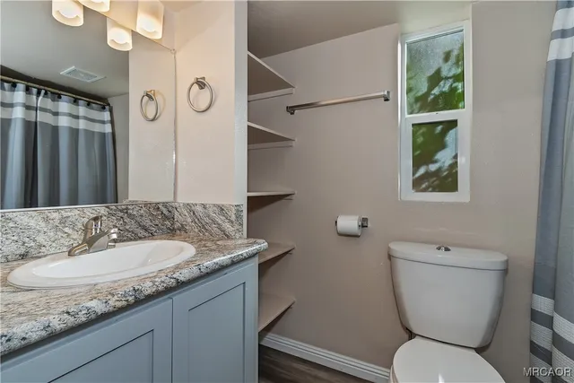 a bathroom with a granite countertop toilet a sink and a mirror