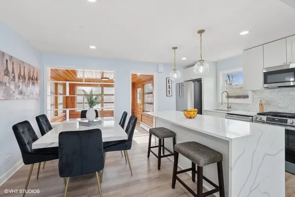 a dining room with stainless steel appliances kitchen island granite countertop a dining table chairs and a refrigerator