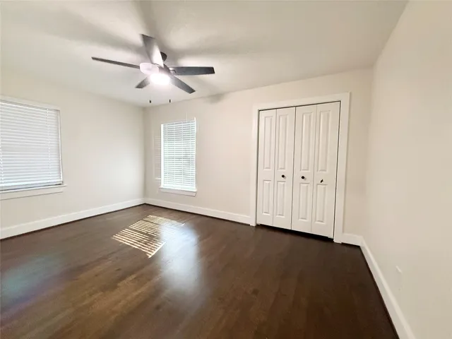 an empty room with wooden floor fan and windows