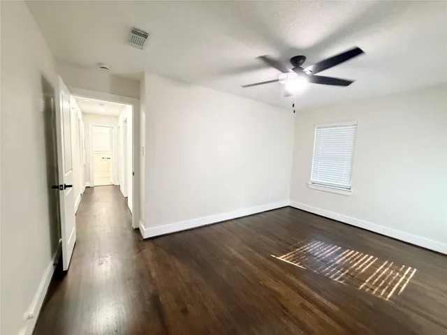 a view of an empty room with wooden floor and a ceiling fan