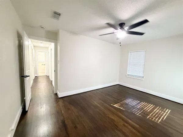 a view of an empty room with wooden floor and a ceiling fan