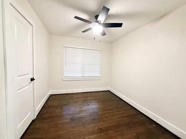 an empty room with wooden floor chandelier fan and windows