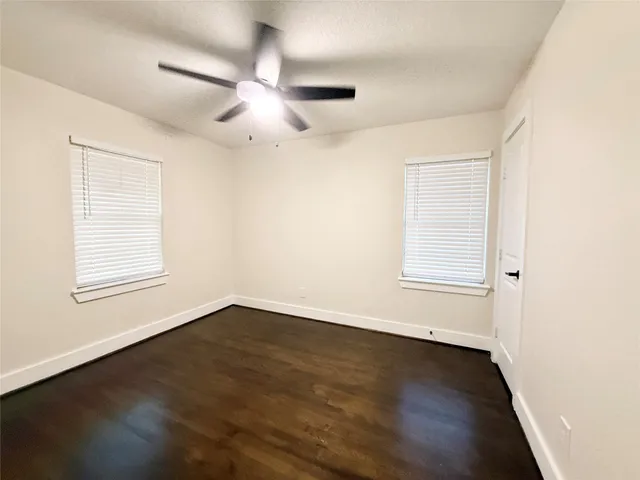 an empty room with wooden floor fan and windows