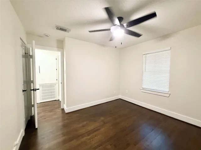 an empty room with wooden floor fan and windows