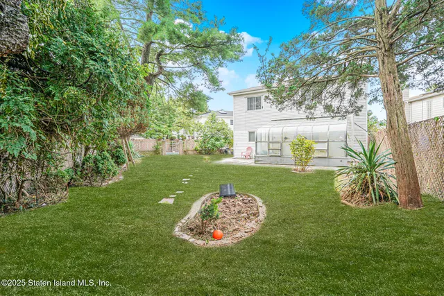 a view of a white house with a big yard and potted plants and large trees