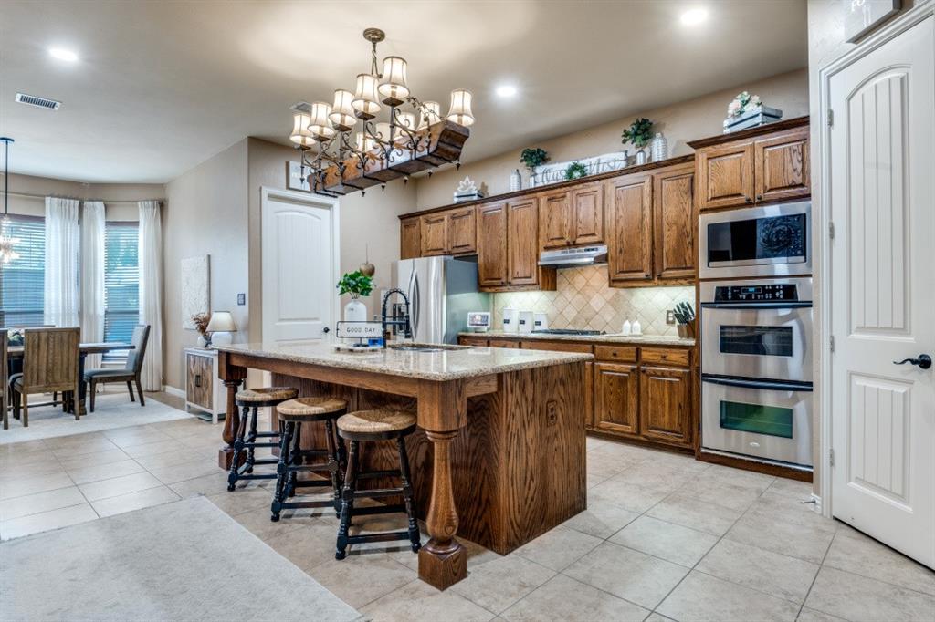2810 Baker Street Sachse, TX 75048 - Photo 8 of 26 Kitchen featuring a chandelier, brown cabinets, a kitchen breakfast bar, a kitchen island with sink, and light tile patterned floors