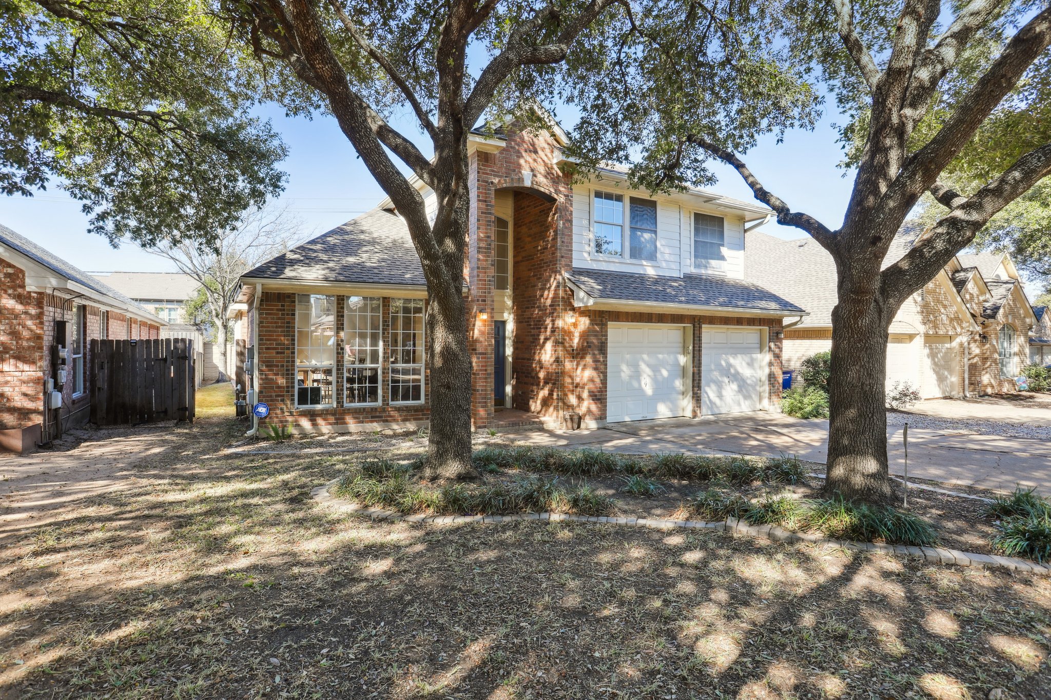 13541 Anarosa Loop Austin, TX 78727 - Photo 2 of 27 Two-story brick and white siding residence featuring an attached two-car garage with white doors, multiple windows, and a prominent brick chimney
