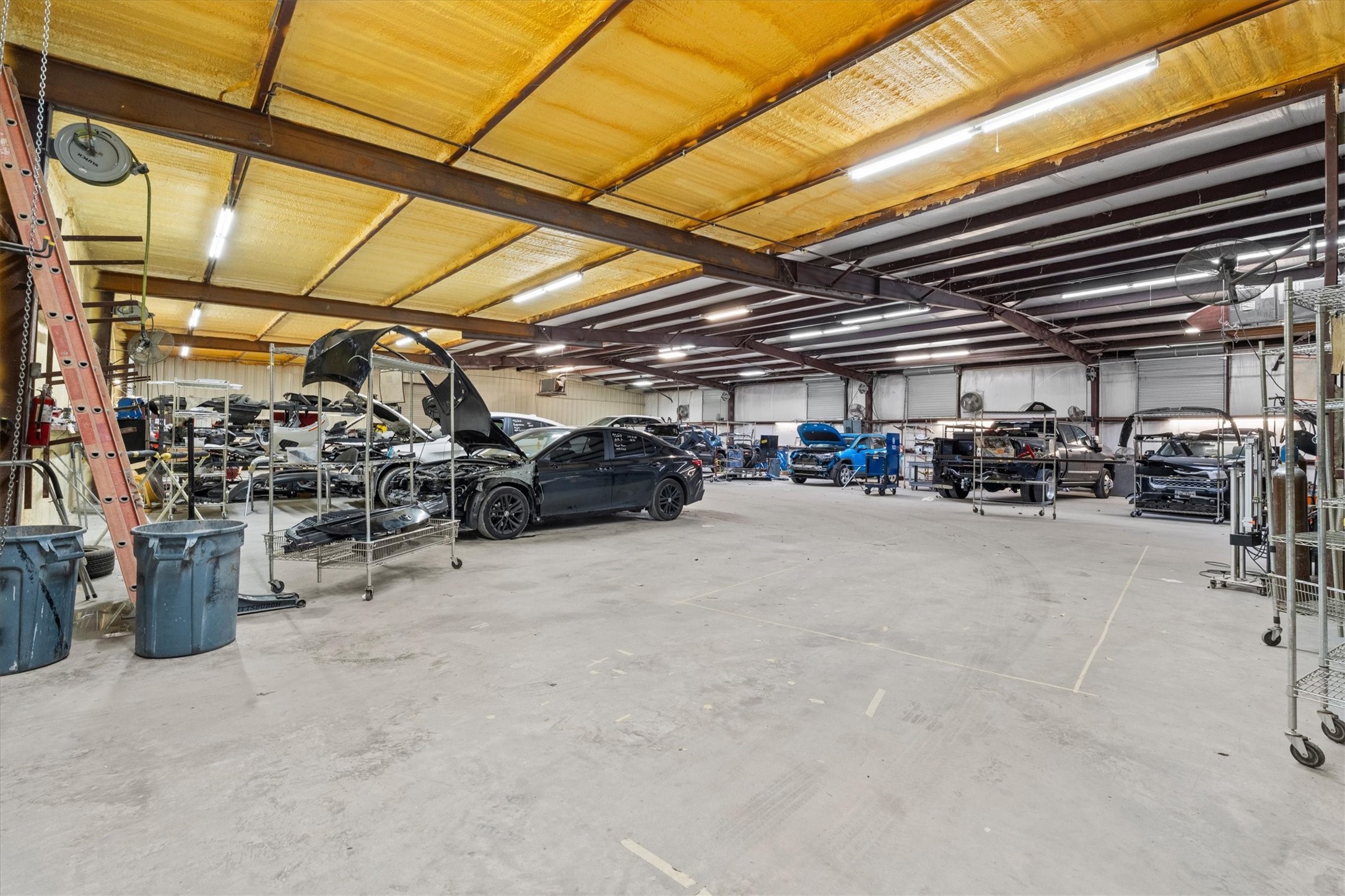 11066 Sh 242 Conroe, TX 77385 - Photo 19 of 21 This photo shows a large, industrial-style garage or workshop with ample space and high ceilings. It's well-lit and houses multiple vehicles, indicating it's suited for automotive work or storage. Ideal for car enthusiasts or business use.