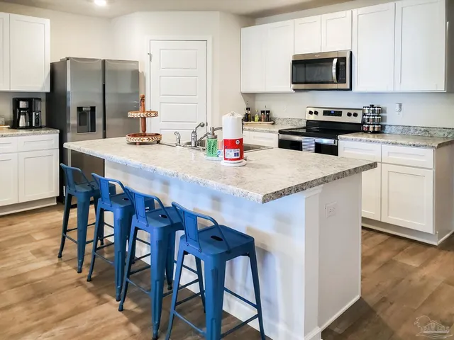 a kitchen with stainless steel appliances a stove a sink a microwave a refrigerator and white cabinets with wooden floor