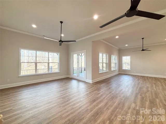 a view of an empty room with wooden floor and fan