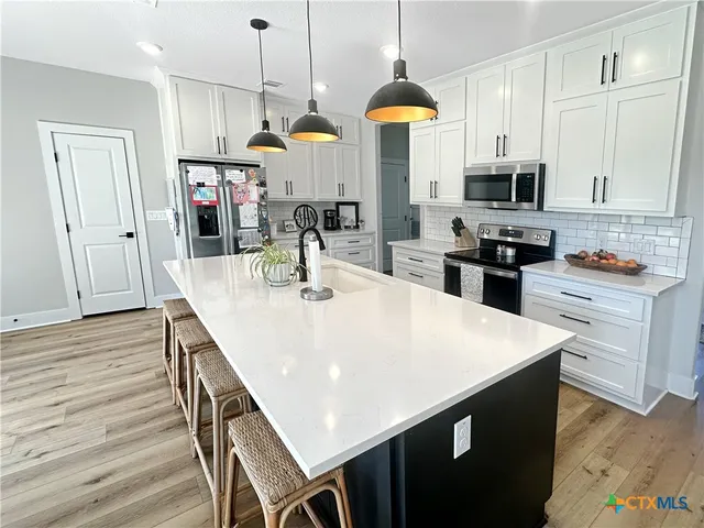a kitchen with stainless steel appliances a stove a sink a kitchen island and chairs with wooden floor
