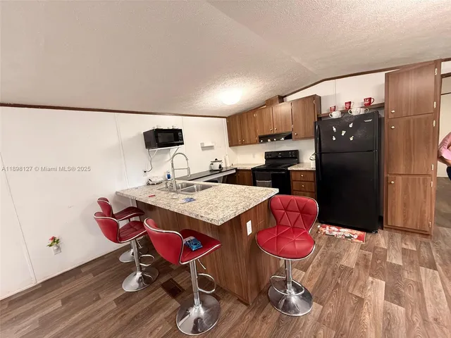 a kitchen with stainless steel appliances kitchen island granite countertop a refrigerator a stove a sink and white cabinets with wooden floor