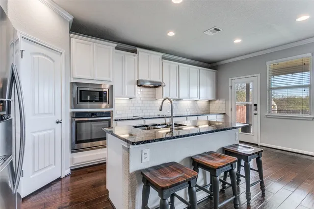 a kitchen with stainless steel appliances granite countertop a stove a refrigerator a sink dishwasher a dining table and chairs with wooden floor