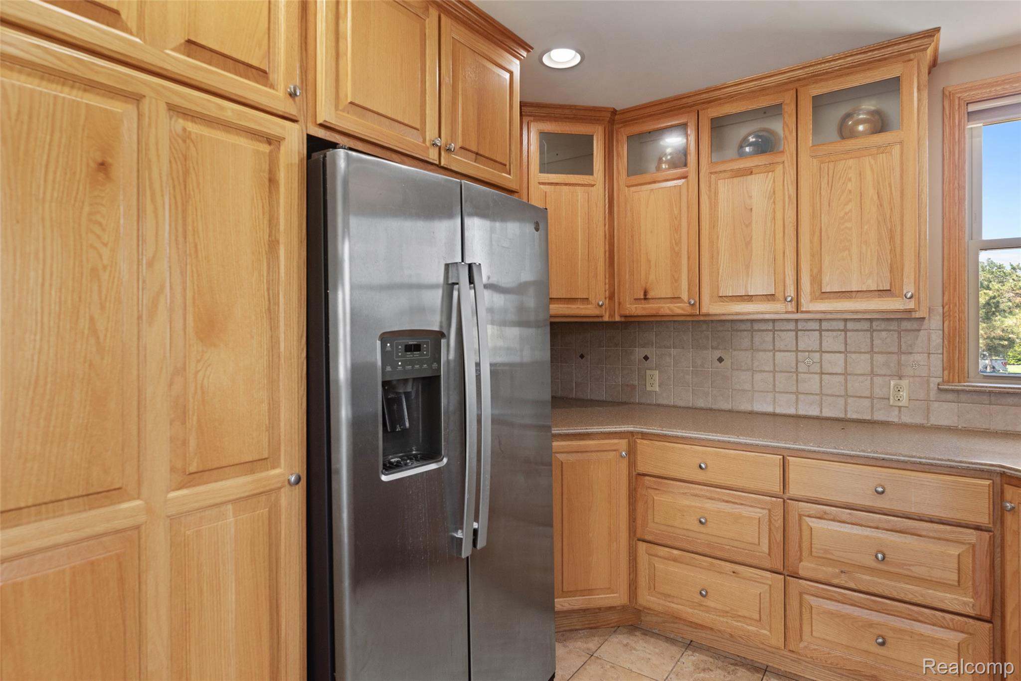 700 Tennyson Rochester, MI 48307 - Photo 13 of 32 Kitchen with stainless steel refrigerator with ice dispenser, recessed lighting, backsplash, light tile patterned floors, and glass insert cabinets