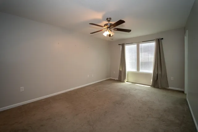 a view of an empty room with chandelier fan and a window