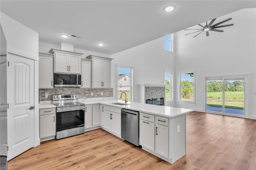 1723 Harris Bridge Road Anderson, SC 29621 - Photo 9 of 33 Modern kitchen with white cabinetry and stainless steel appliances flows into an open living space with soaring ceilings and a cozy fireplace.