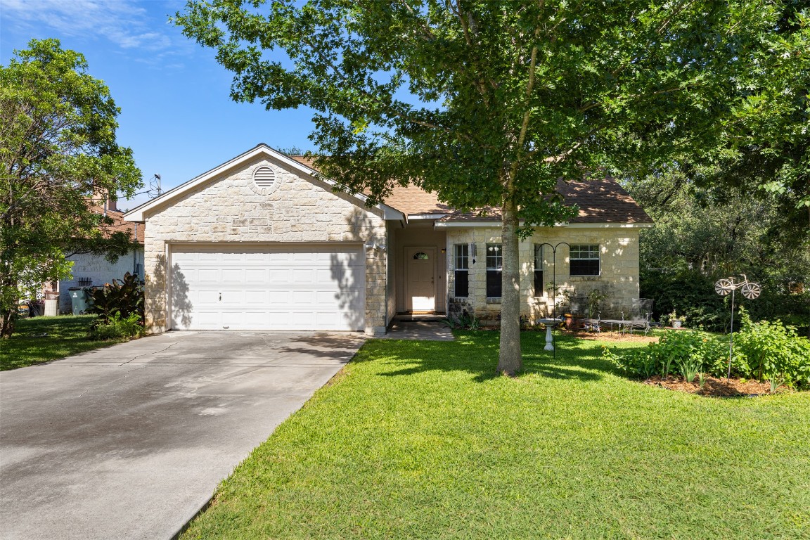 Ranch-style home featuring a garage, a front yard, concrete driveway, and stone siding