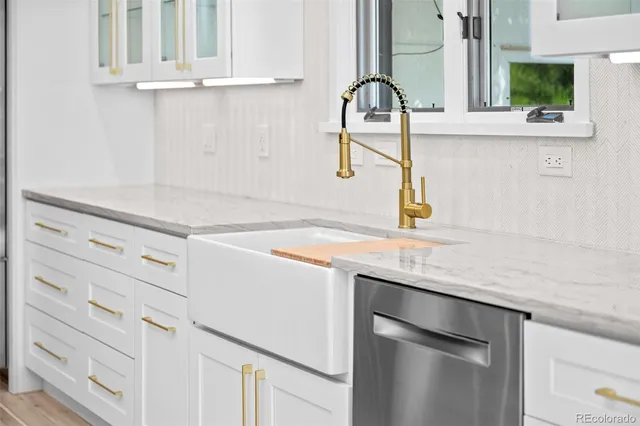 a large white kitchen with granite countertop a stove oven a sink dishwasher and white cabinets with wooden floor