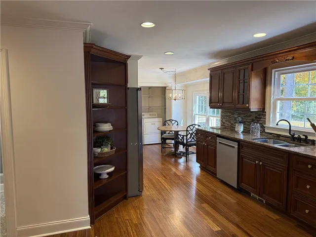 a kitchen with stainless steel appliances granite countertop a refrigerator a sink dishwasher a stove and a dining table with wooden floor