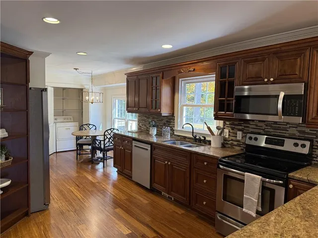 a kitchen with stainless steel appliances granite countertop a stove top oven a sink dishwasher a dining table and chairs with wooden floor