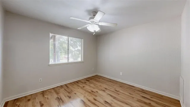 an empty room with wooden floor fan and windows