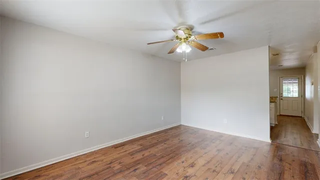 a view of an empty room with wooden floor and a ceiling fan