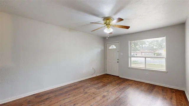 an empty room with wooden floor fan and windows