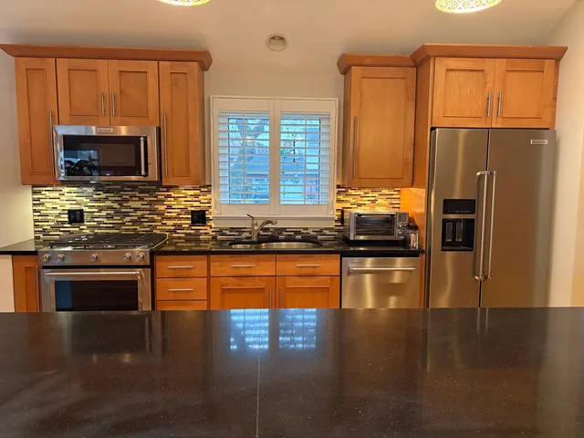 a kitchen with stainless steel appliances granite countertop a refrigerator a stove top oven a sink dishwasher and wooden cabinets with wooden floor