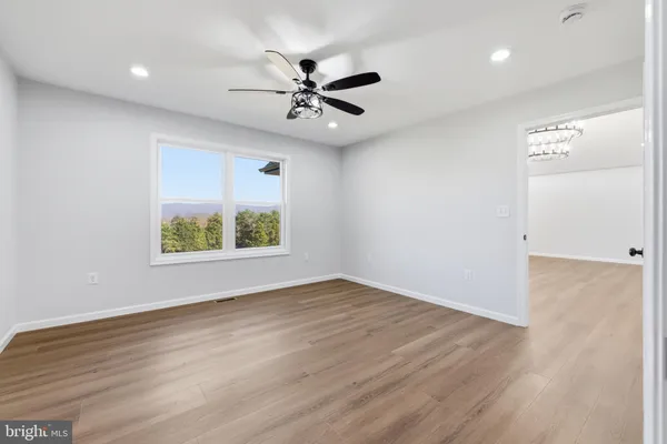 an empty room with wooden floor ceiling fan and windows