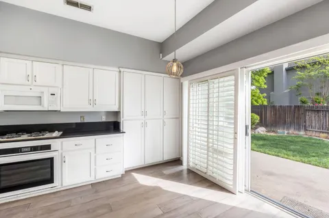 a kitchen with granite countertop a stove a sink and white cabinets with wooden floor