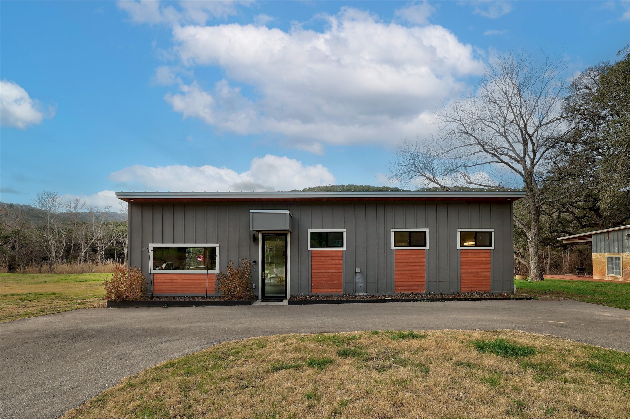 7001 Ranch Road 2222 Austin, TX 78730 - Photo 17 of 18 A striking modern exterior combines corrugated metal with warm wood accents, set against a verdant, hilly backdrop.