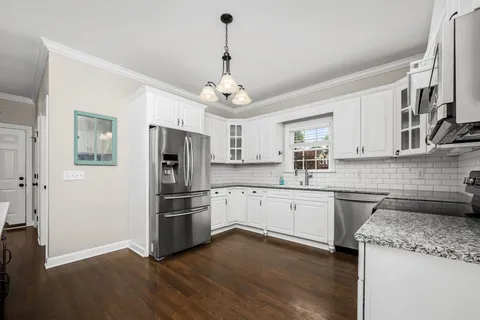 a kitchen with stainless steel appliances granite countertop a refrigerator a stove a sink dishwasher a oven with white cabinets and wooden floor