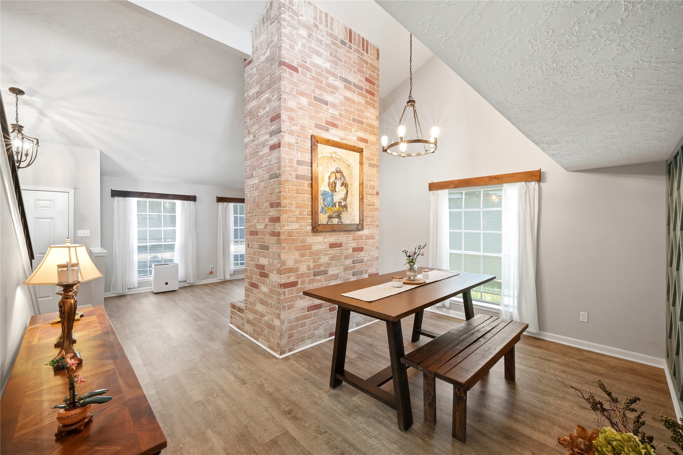 4718 Temple Bell Drive Spring, TX 77388 - Photo 9 of 50 This room features a bright, open layout with large windows, a striking brick pillar, and a vaulted ceiling. It includes a cozy dining area with a wooden table and bench, and light wood flooring, creating a warm, inviting atmosphere.