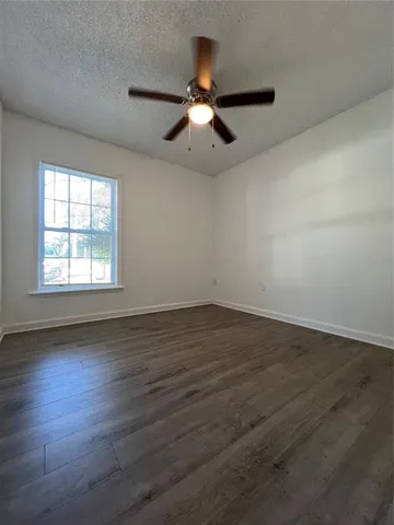 an empty room with wooden floor ceiling fan and windows