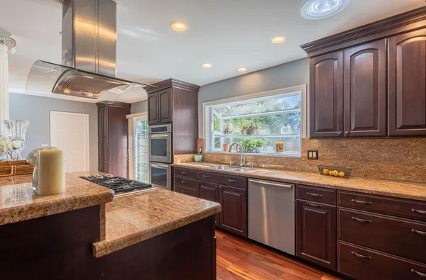 a kitchen with kitchen island granite countertop a sink stainless steel appliances wooden floor and a counter top space