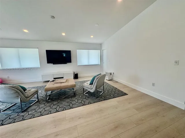 a living room with furniture a flat screen tv and a refrigerator