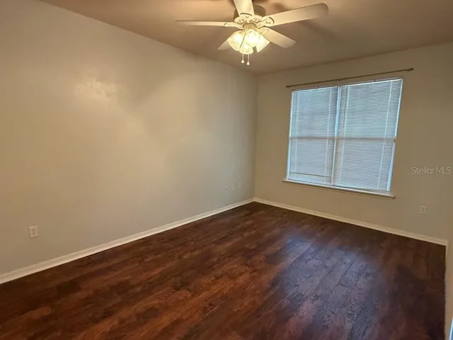 an empty room with wooden floor fan and windows