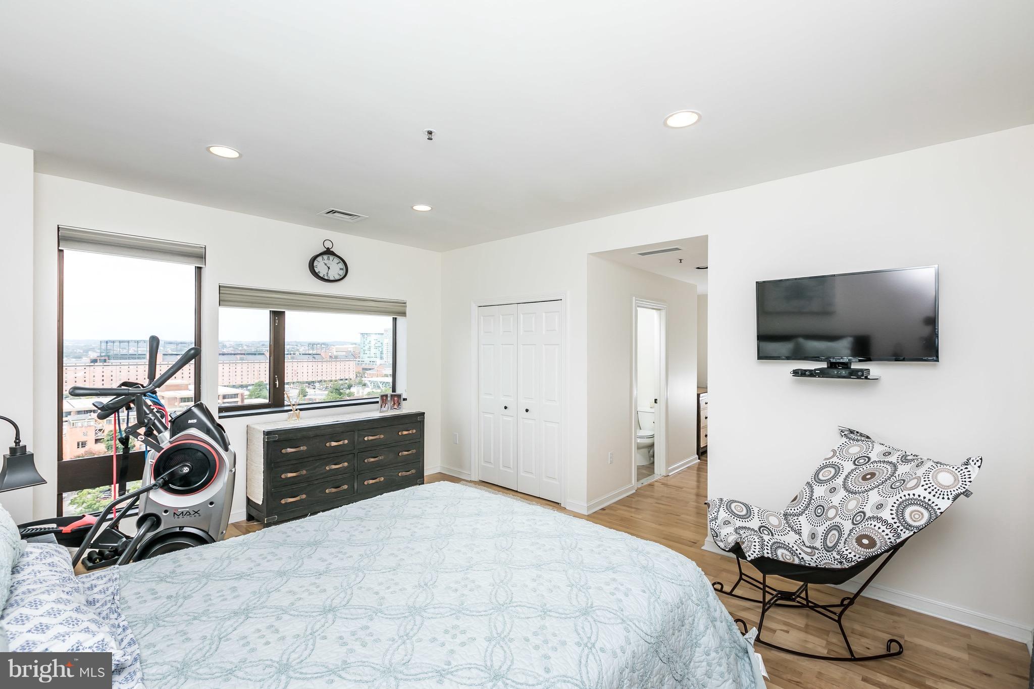 10 East Lee Street, Unit 1209 Baltimore, MD 21202 - Photo 19 of 38 a bedroom with a bed and a flat tv screen on the dresser