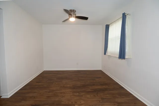 an empty room with wooden floor fan and windows