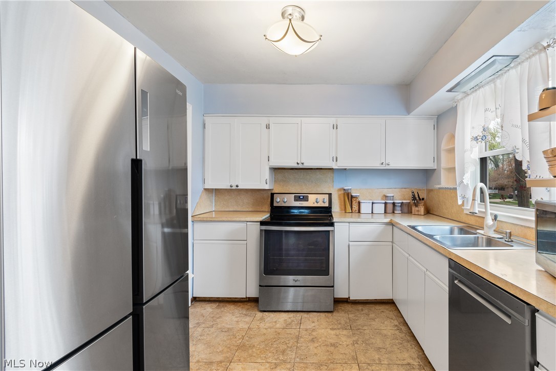 1256 Garman Road Akron, OH 44313 - Photo 12 of 32 Kitchen with appliances with stainless steel finishes, light tile floors, white cabinets, sink, and tasteful backsplash