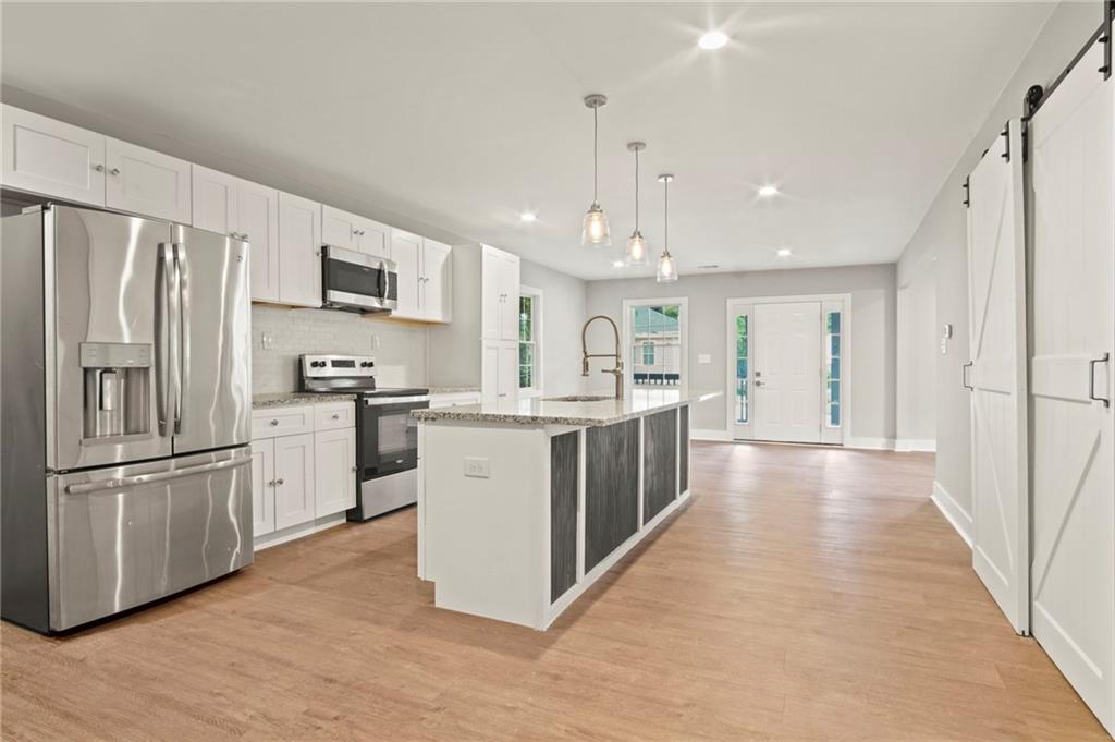 a kitchen with stainless steel appliances granite countertop a refrigerator a sink dishwasher a s stove top oven a refrigerator and white cabinets with wooden floor