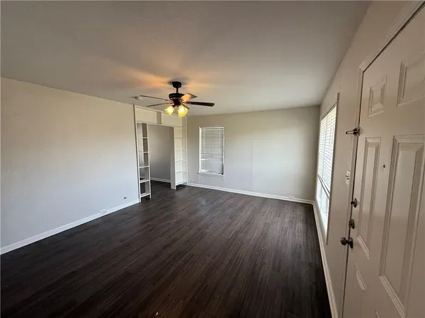 a view of an empty room with wooden floor and a ceiling fan