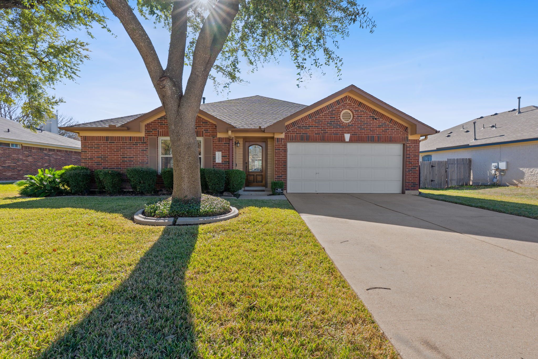 Ranch-style home with a front yard, concrete driveway, brick siding, a garage, and a shingled roof