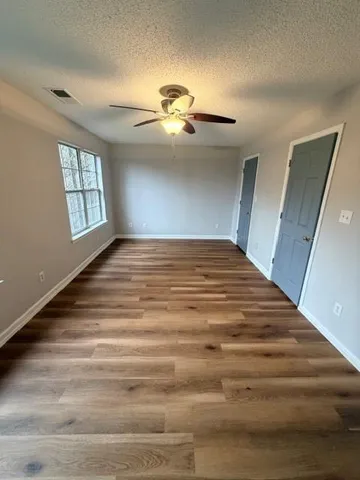 a view of empty room with wooden floor and fan