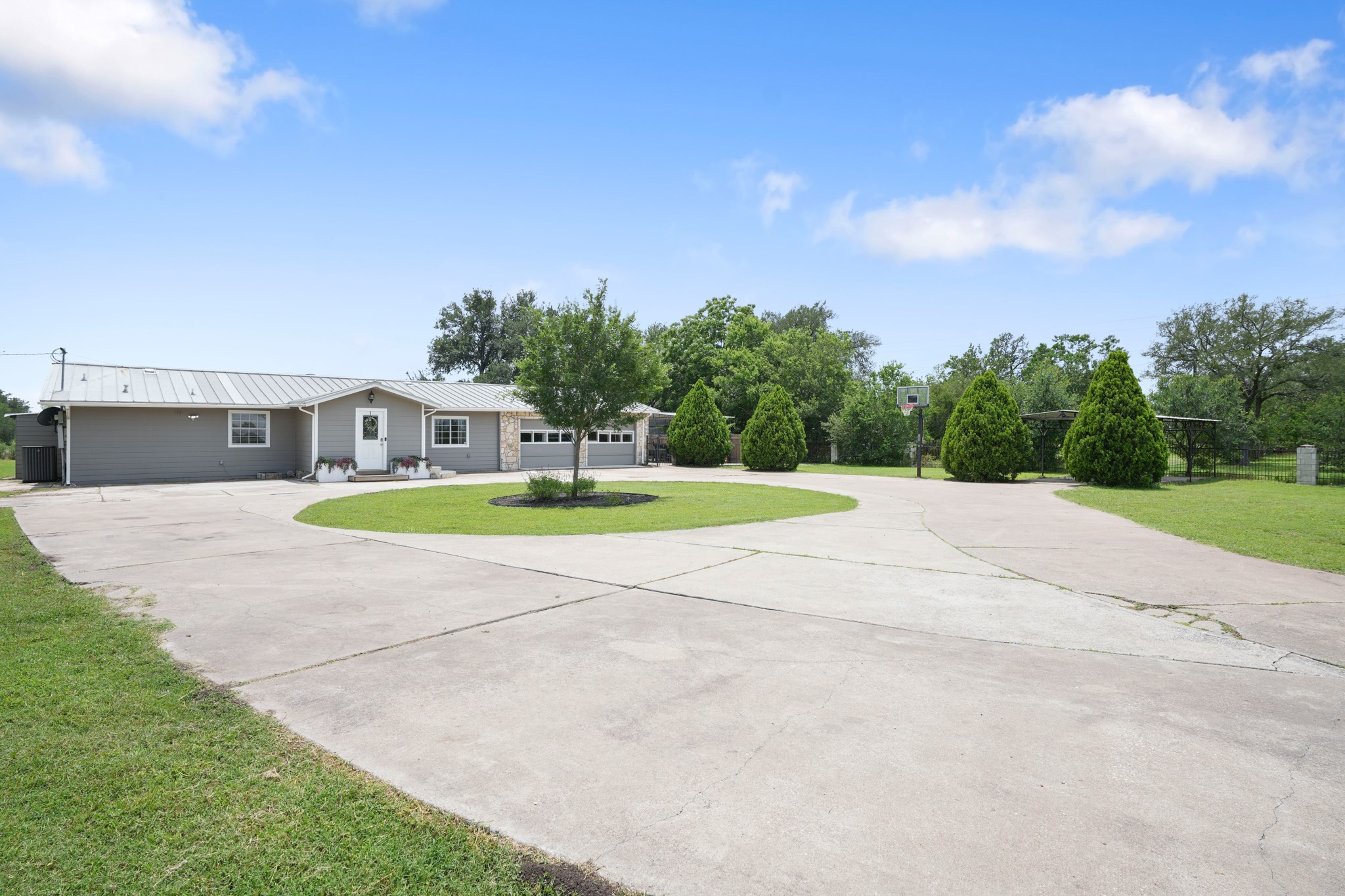 9725 Bock Road Buda, TX 78610 - Photo 26 of 32 A spacious concrete driveway provides ample parking and leads to a charming gray home with a welcoming front entrance.