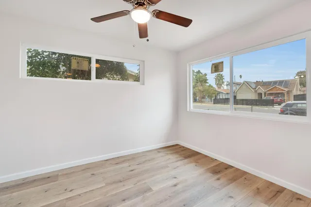 an empty room with wooden floor fan and windows