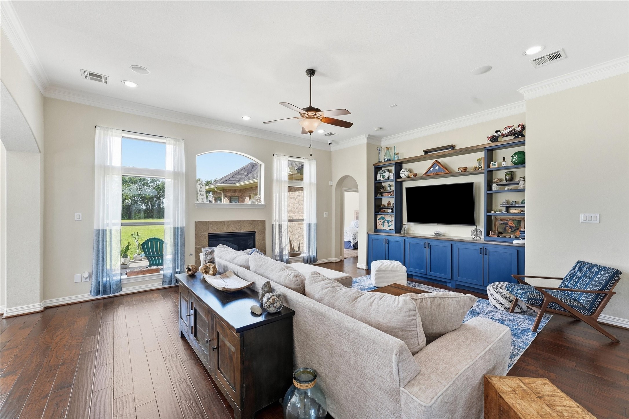 4810 Magnolia Bend Drive Rosharon, TX 77583 - Photo 9 of 40 Spacious living room featuring elegant hardwood floors, a cozy fireplace, and built-in shelving with a vibrant blue finish. Large windows offer abundant natural light and a charming view of the lush backyard.