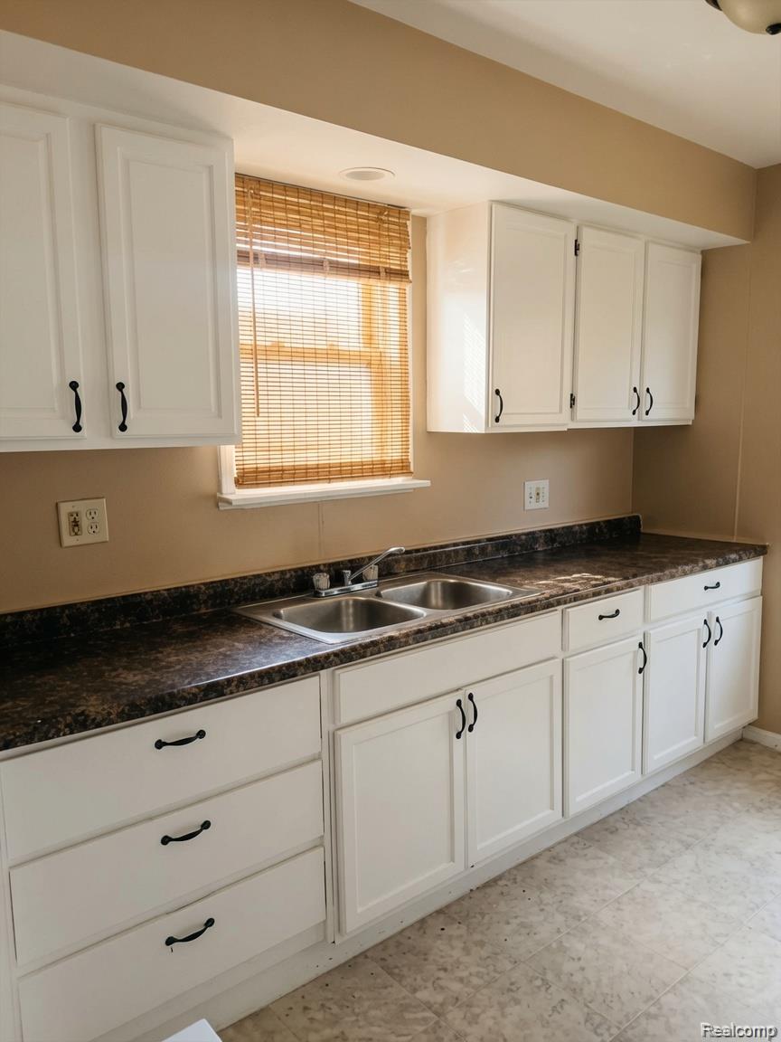 16069 Liberal Street Detroit, MI 48205 - Photo 9 of 9 Kitchen featuring a double basin stainless steel sink, white cabinetry with black hardware, and dark patterned countertops