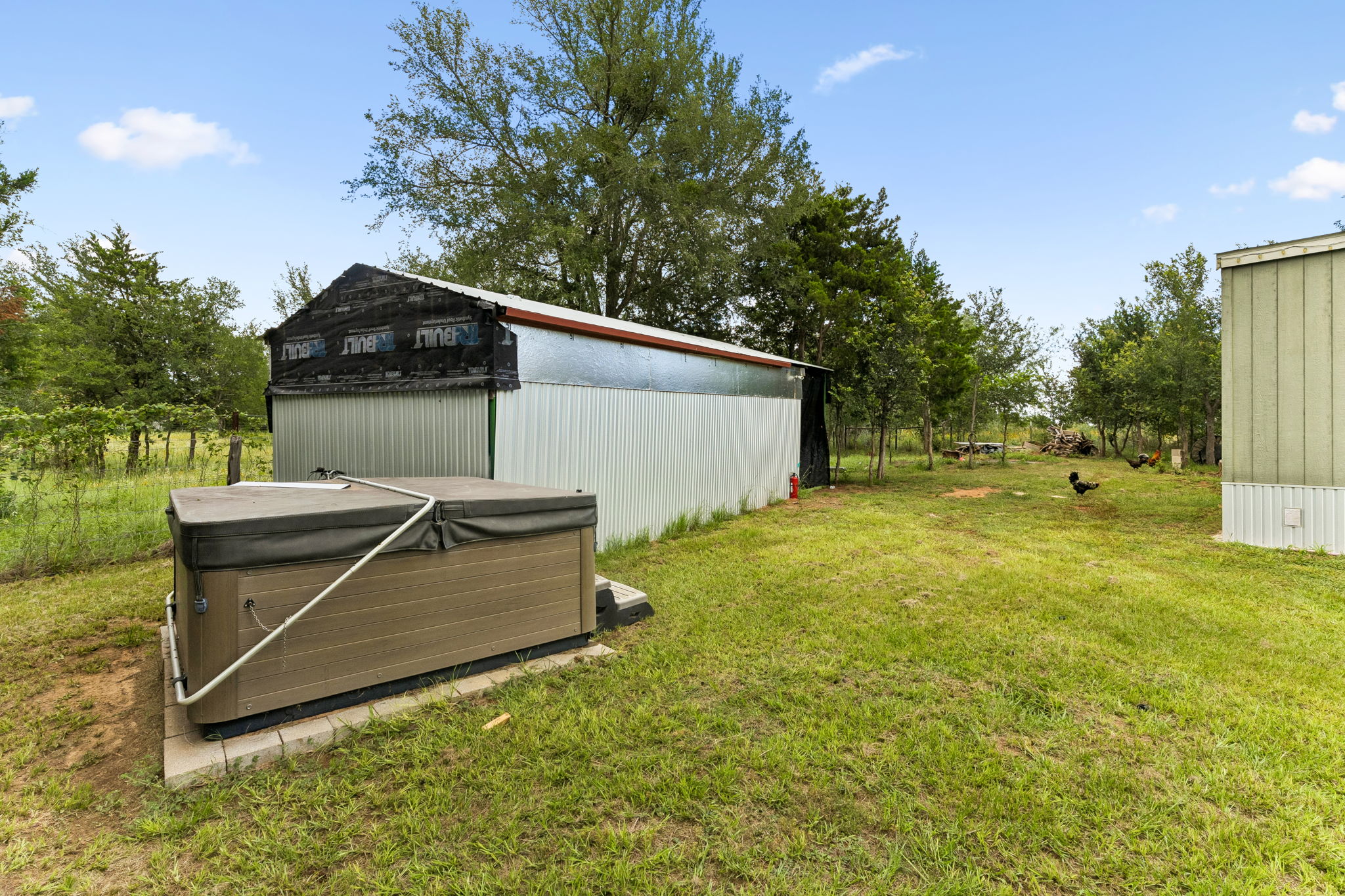 253 North County Line Road, Unit C Elgin, TX 78621 - Photo 28 of 39 A spacious backyard features a spa, a metal outbuilding, and mature trees.